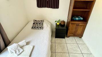 Une petite chambre à coucher, bien rangée, avec un lit simple, une table de chevet, une armoire en bois et un élément décoratif fixé au mur.