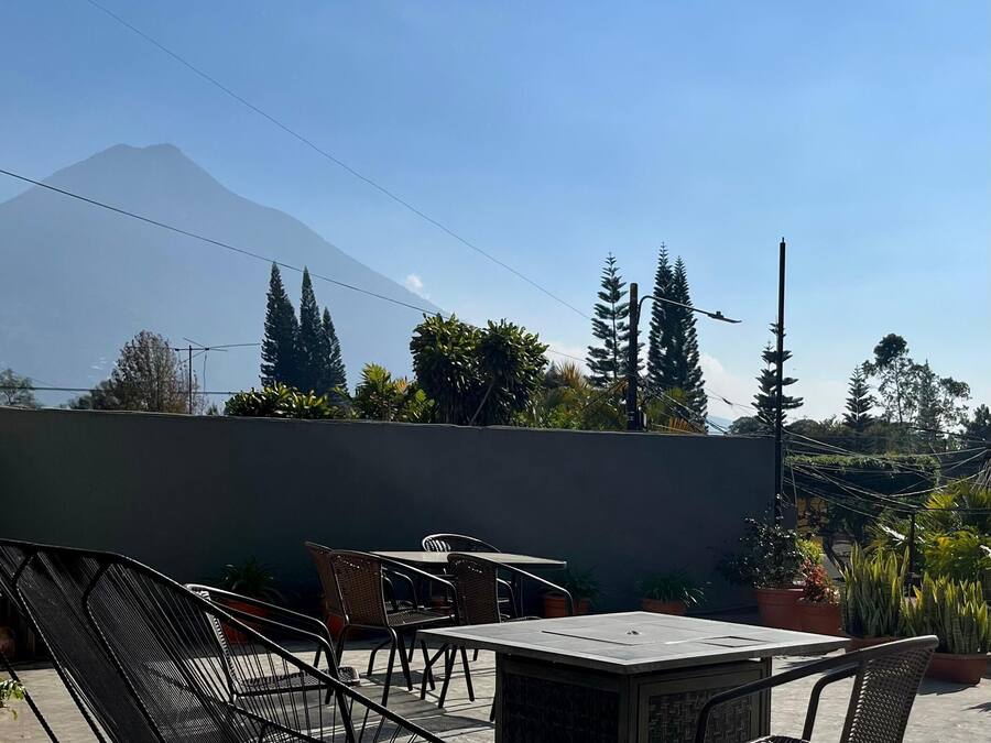 A rooftop patio with a table and chairs, surrounded by potted plants and overlooking a mountain.