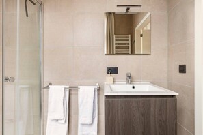 A modern bathroom with a glass shower enclosure, a white sink, and a mirror above it.