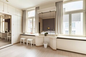 A modern bedroom with a large window, a bedside table, a mirror, and a wardrobe.