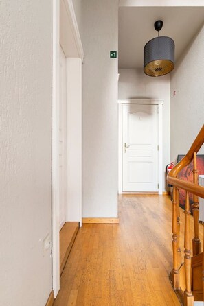 Un pasillo con piso de madera, una puerta blanca y una escalera con barandillas de madera.