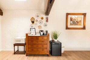 Una habitación con un aparador de madera, una mesita con microondas, un refrigerador negro y un cuadro en la pared.