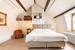 A bedroom with a sloped ceiling, a bed, a chair, a bedside table, and a window.