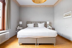 A bedroom with a large bed, two bedside tables, a radiator, and a window.
