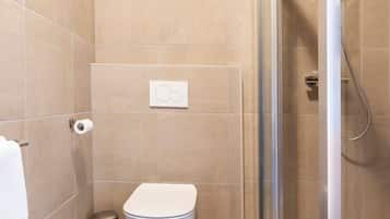 Ein Badezimmer mit Toilette, Mülleimer und einer Duschkabine.