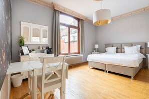Ein Hotelzimmer mit einem Bett, einem Schreibtisch, einem Sessel, einem Heizkörper und einem Fenster mit Vorhängen.