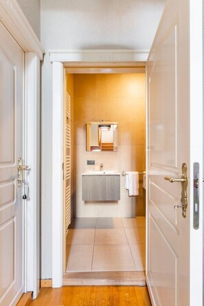A narrow hallway leading to a bathroom with a sink, mirror, and towel rack.