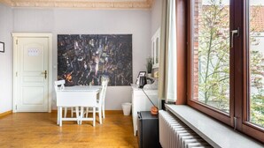 A room with a dining table, chairs, a radiator, a window with a view of trees, and a large abstract painting on the wall. - ROOM N°1 / City Center Spacious King Suite * Private External Bathroom (Brugge)