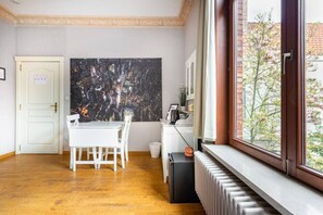 A room with a dining table, chairs, a radiator, a window with a view of trees, and a large abstract painting on the wall. - ROOM N°1 / City Center Spacious King Suite * Private External Bathroom (Brugge)