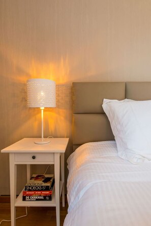 A bed with a headboard, a bedside table with a lamp, and a shelf with books.