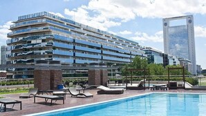 A modern hotel with a rooftop pool, multiple balconies, and a view of a tall building in the background. - Puerto Madero Piso 20 Vista al Rio  (Buenos Aires)