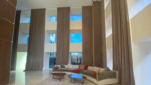 A spacious living area with a large sofa, two coffee tables, and a view of a modern building through large windows. - Puerto Madero Piso 20 Vista al Rio  (Buenos Aires)