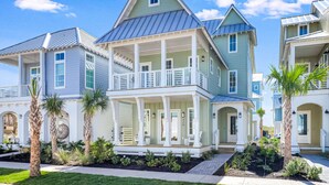 A multi-story residential building with a porch, multiple windows, and a well-maintained garden with palm trees. - Multi-level home with beach access, outdoor pool, outdoor shower, balcony (Port Aransas)