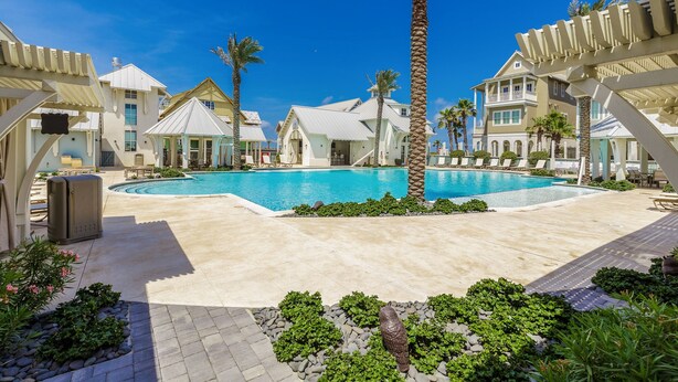A pool area with a clear blue pool, surrounded by palm trees and lounge chairs. - Multi-level home with beach access, outdoor pool, outdoor shower, balcony (Port Aransas)