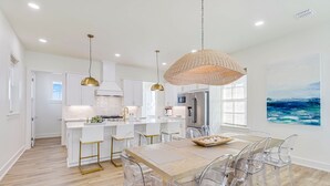A modern kitchen with white cabinets, a wooden island, and a dining area with clear chairs. - Multi-level home with beach access, outdoor pool, outdoor shower, balcony (Port Aransas)