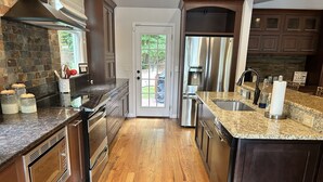 A modern kitchen with granite countertops, stainless steel appliances, and wooden flooring. - Lakefront Home for Spring and Summer Getaways! (Eatonton)
