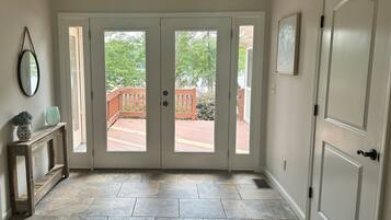 A hallway with a double door leading to an outdoor deck, a wooden console table with a vase, and a clock on the wall.