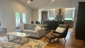 A spacious living room with a grey sectional sofa, a brown leather armchair, and a coffee table. There is a wooden floor and a patterned rug. - Lakefront Home for Spring and Summer Getaways! (Eatonton)