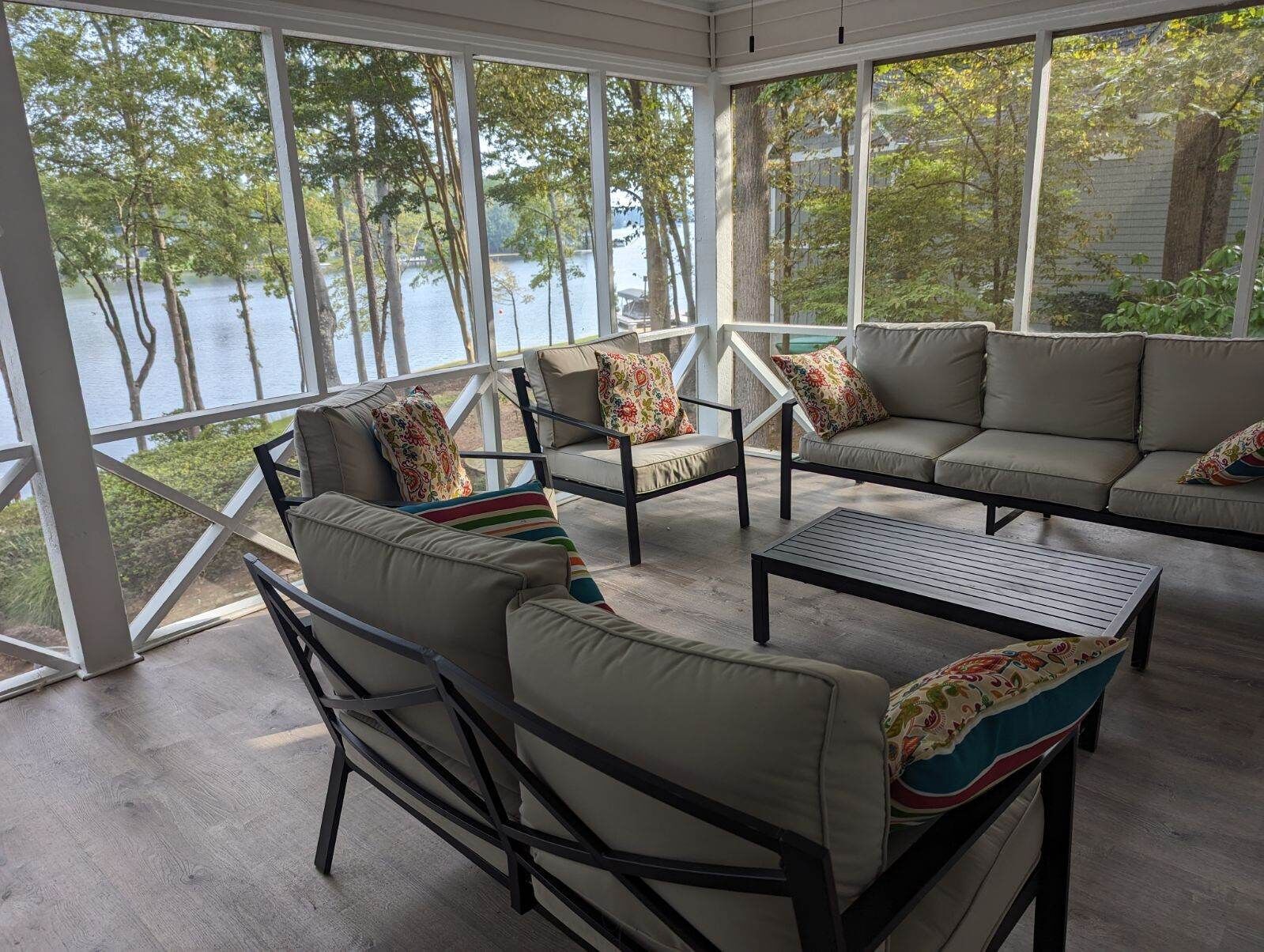 En solbeskinnet veranda med udsigt over en sø, med en sofa, stole og et sofabord.