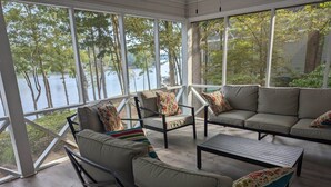 A sunlit porch with a view of a lake, featuring a sofa, chairs, and a coffee table. - Lakefront Home for Spring and Summer Getaways! (Eatonton)