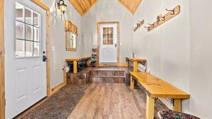 Un hall d’entrée spacieux avec un plafond en bois, une porte blanche et un espace avec un banc et une petite table.
