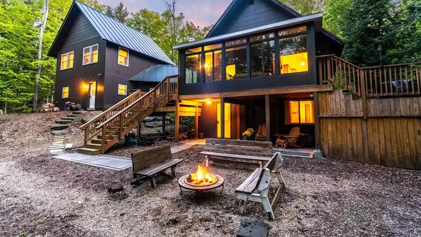 Une cabane moderne à deux étages dotée d’une terrasse, d’un foyer extérieur et de meubles de jardin.