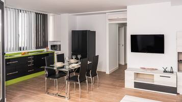 A modern kitchen with black cabinets, a dining table with chairs, and a flat-screen TV mounted on the wall.