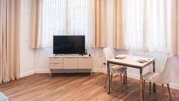 Een moderne woonkamer met een flatscreen televisie op een wit kastje, een eettafel met stoelen en een bank.