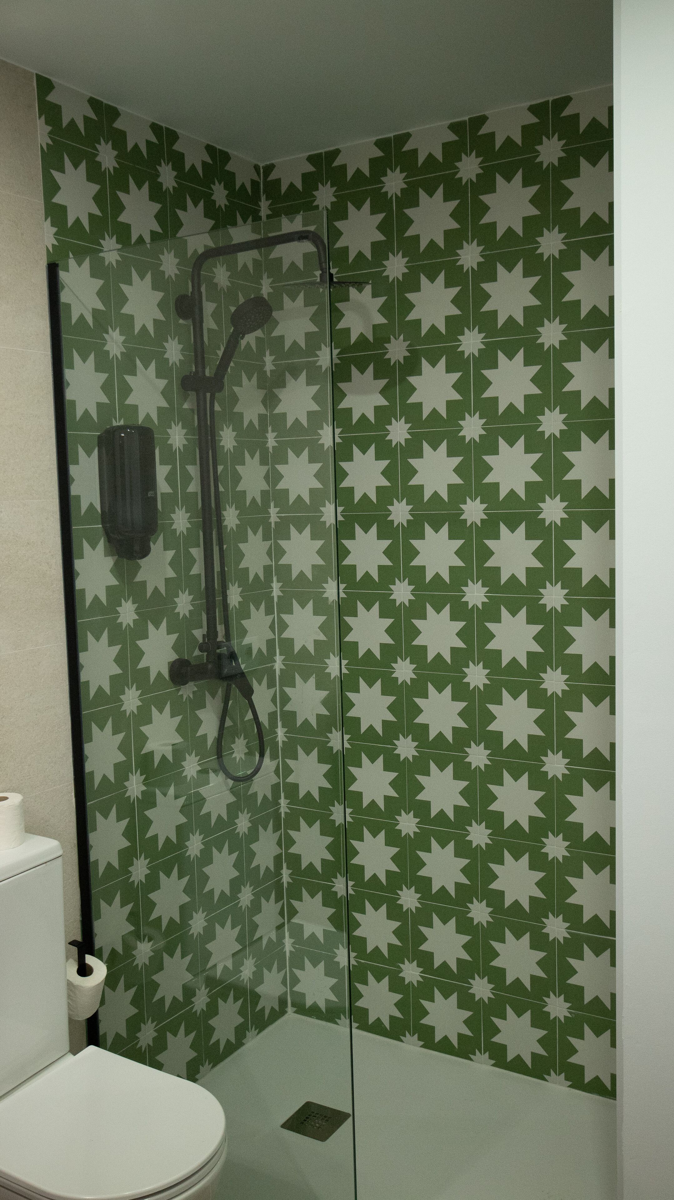 A bathroom with a shower, toilet, and a green star-patterned wall.