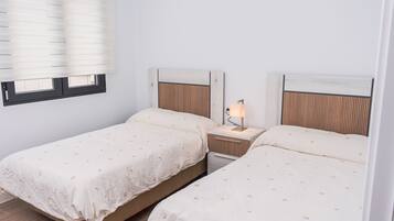 A twin room with two beds, a nightstand with a lamp, and a window with blinds.