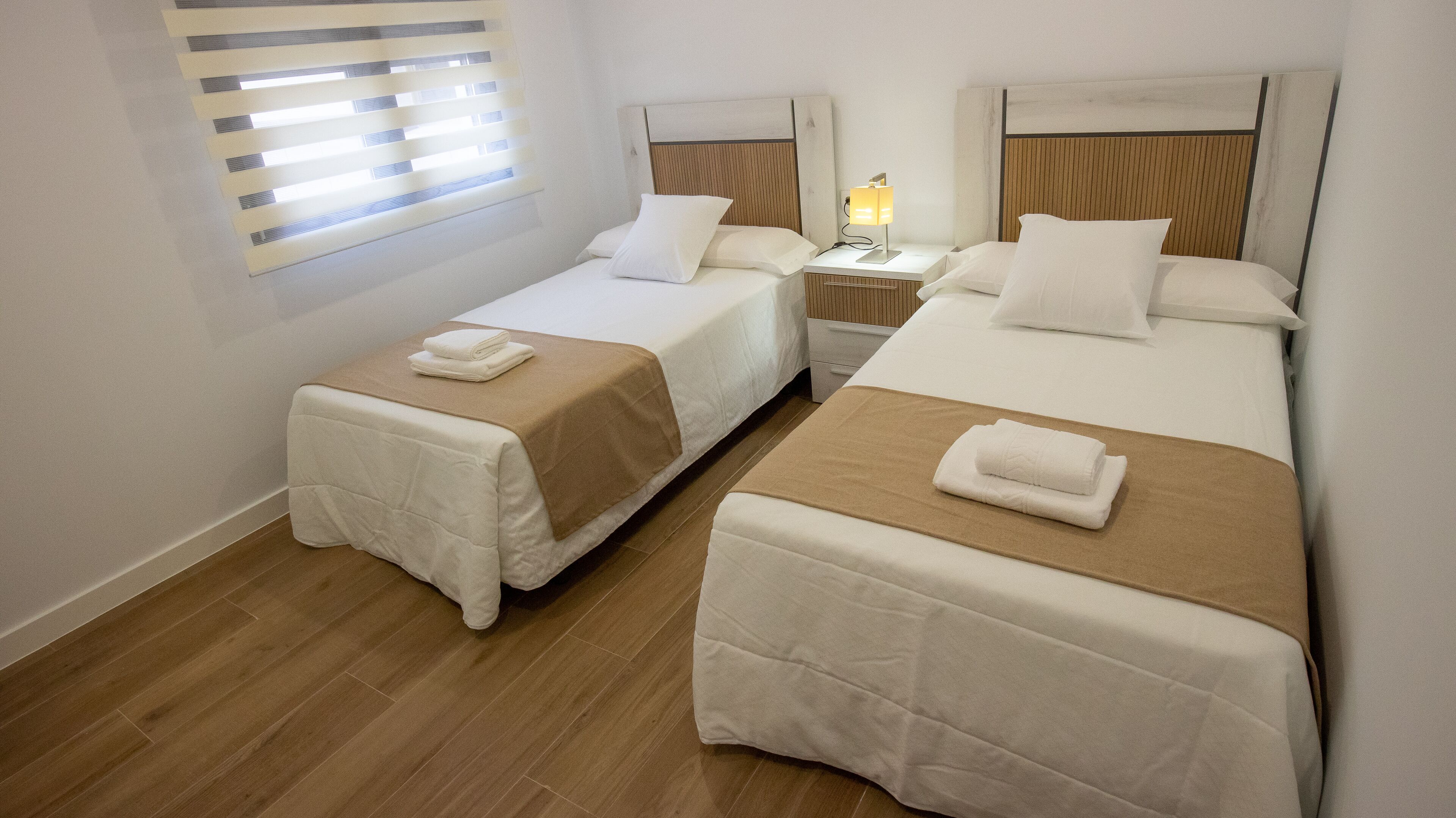 Une chambre d’hôtel avec deux lits simples, chacun recouvert d’une couverture marron et agrémenté d’oreillers blancs, ainsi qu’une petite table de chevet avec une lampe.