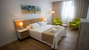 A hotel room with a large bed, two bedside tables with lamps, a painting on the wall, and two green armchairs. - Alojamientos VEN, Vista Extremadura Norte (Plasencia)
