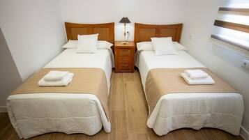 Ein Doppelzimmer mit zwei Betten, jeweils mit einem Holz-Kopfteil, einem Nachttisch dazwischen und einer Lampe auf dem Nachttisch.