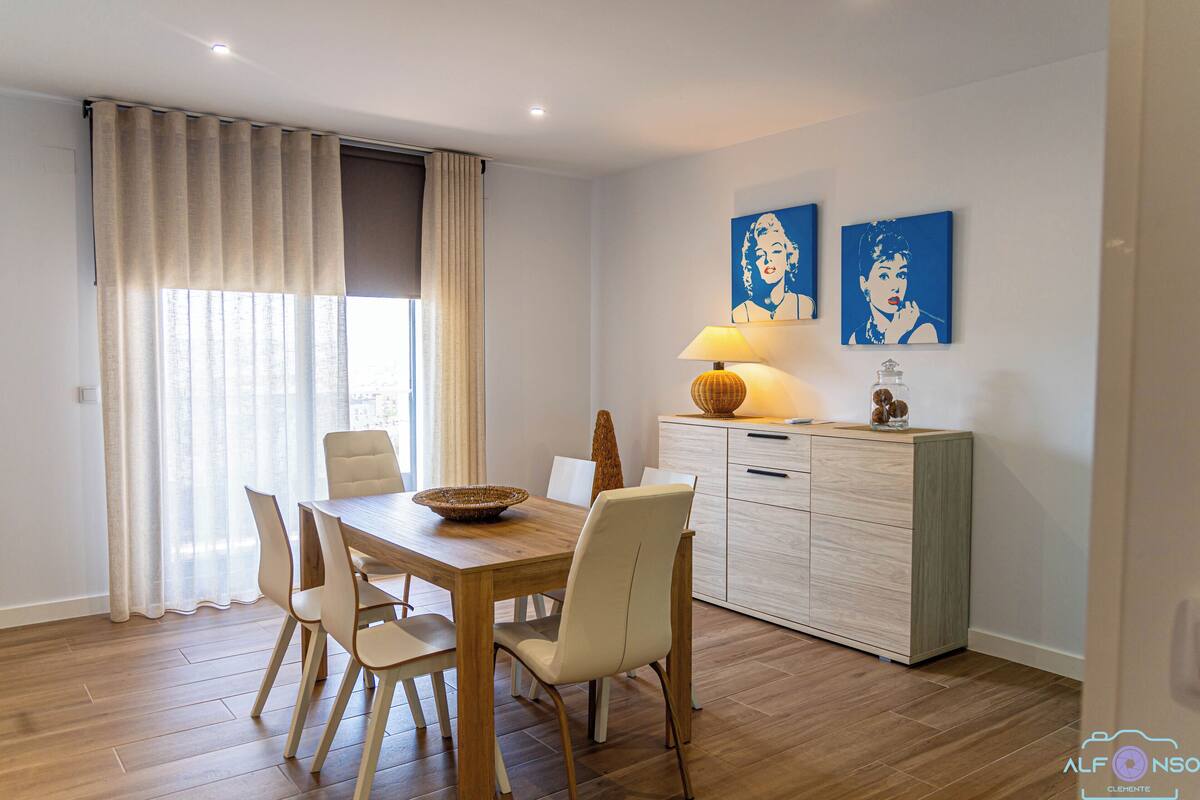 A dining area with a wooden table, white chairs, a lamp, and a cabinet.