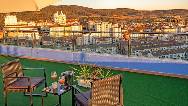 A rooftop terrace with two wicker chairs, a table with drinks, and a large umbrella. - Alojamientos VEN, Vista Extremadura Norte (Plasencia)