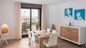 A dining room with a large table, white chairs, a wooden cabinet, and a view of the city through a large window. - Alojamientos VEN, Vista Extremadura Norte (Plasencia)