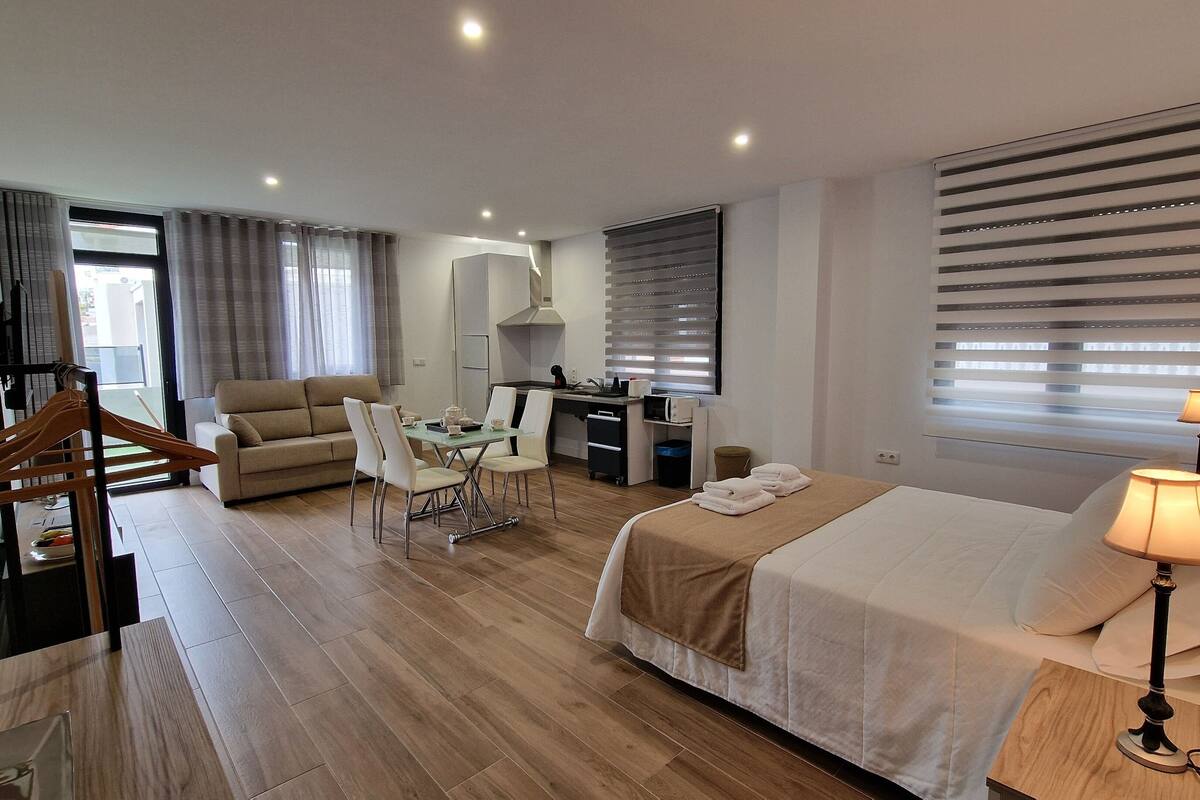 A hotel room with a bed, bedside lamp, desk, chair, and a sofa.