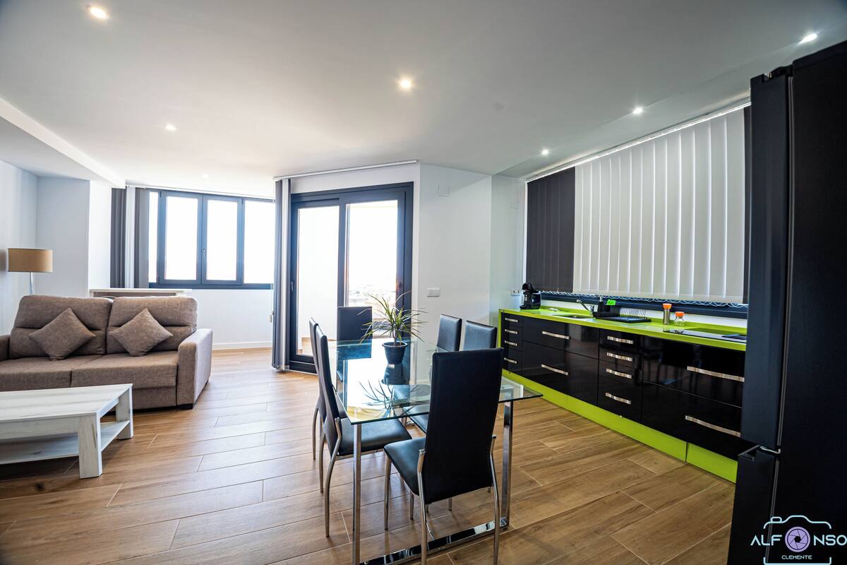 A modern living room with a glass dining table, black chairs, and a beige sofa.