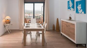 Un coin repas avec une table dressée pour quatre personnes, un buffet en bois et une vue sur la ville grâce à de grandes fenêtres.