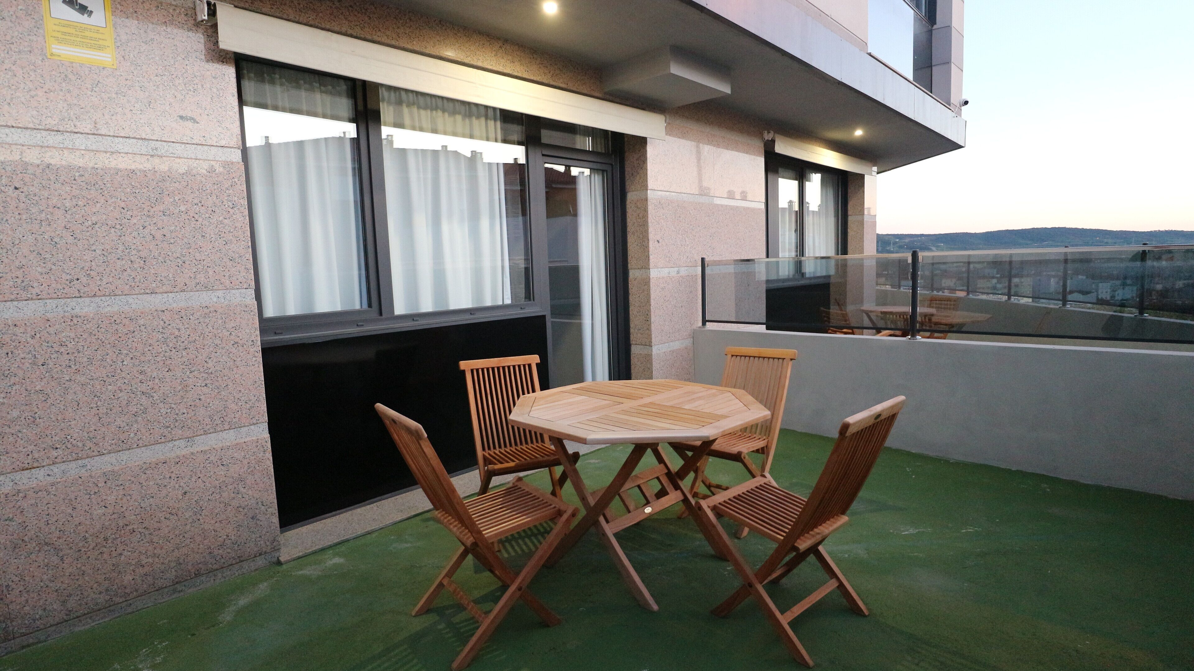 A balcony with a table and chairs, a view of the city, and a building facade with a stone exterior.