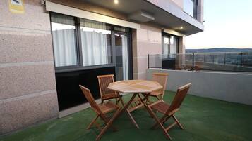 A balcony with a table and chairs, a view of the city, and a building facade with a stone exterior.
