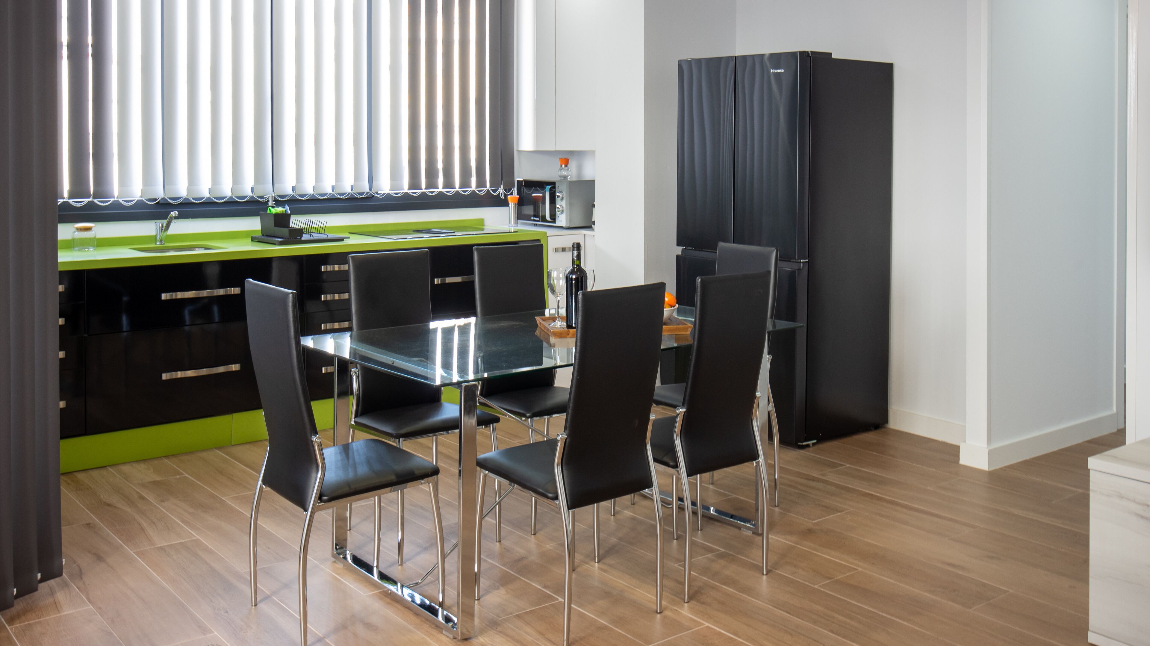 Una cocina moderna con zona de comedor, que incluye un refrigerador negro, un microondas y una encimera verde.