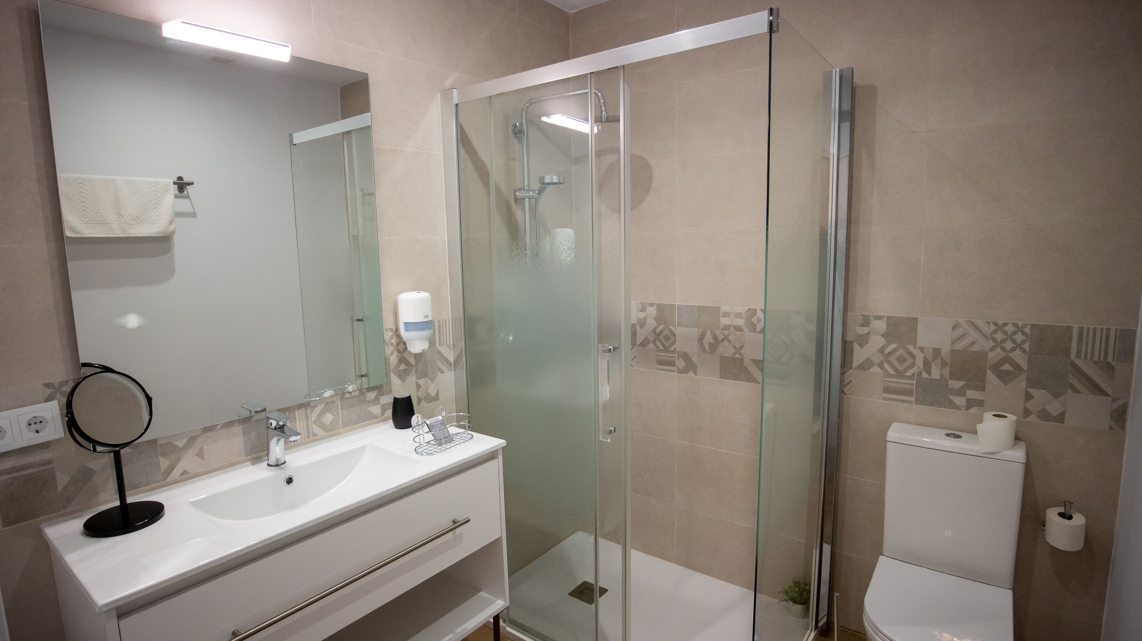 Un bany modern amb dutxa de vidre, un lavabo blanc i un vàter.