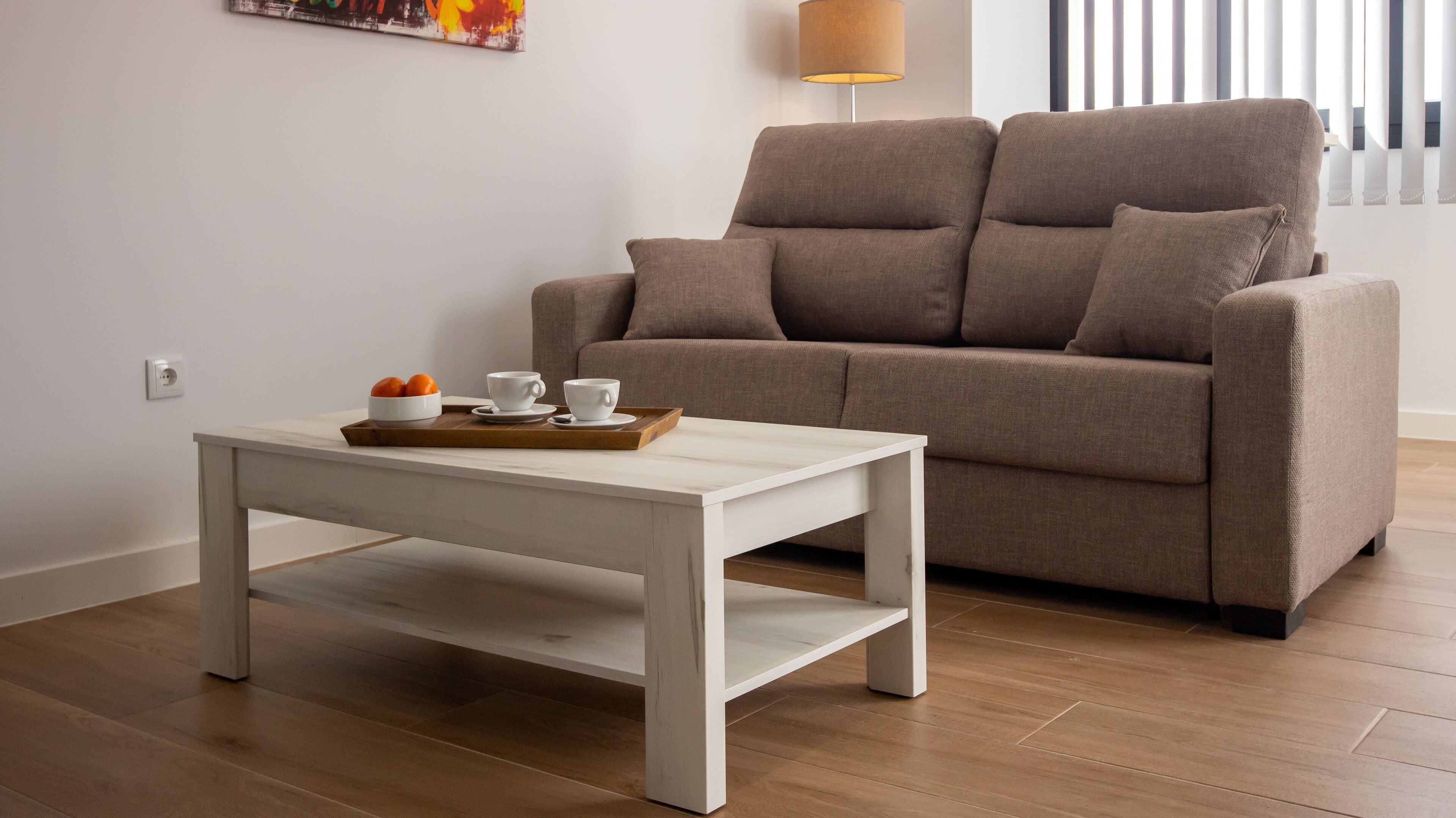 A modern living room with a white coffee table, a brown sofa, and a tray with oranges and cups.