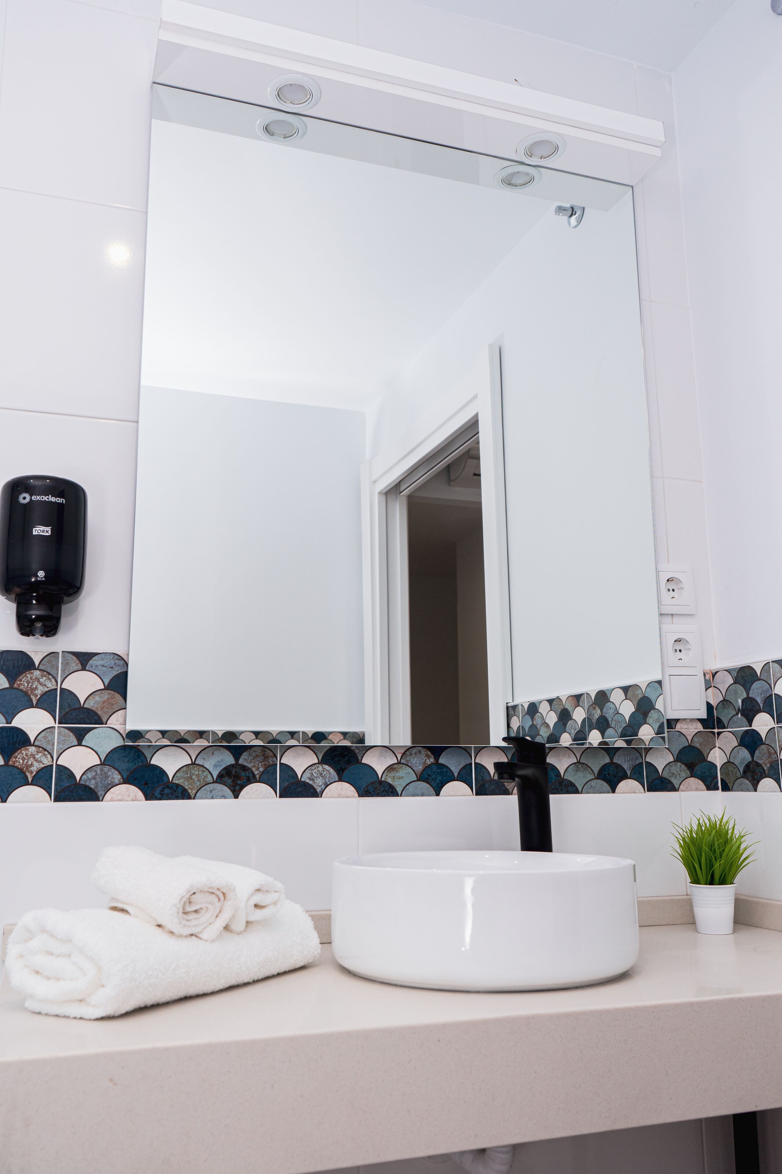A bathroom with a white sink, a mirror, a towel rack, a hand dryer, and a potted plant.