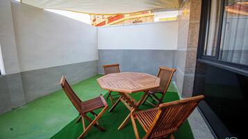 Un patio con una mesa redonda de madera y cuatro sillas, rodeado de un piso de césped artificial verde y paredes blancas.