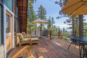 A wooden deck with outdoor furniture, a table, and umbrellas, overlooking a forest and a body of water. - Pet Friendly with Big Views! (Tahoe City)