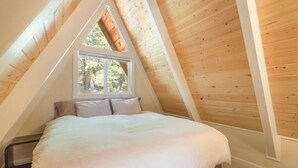 A bedroom with a sloped ceiling, a large window, and a bed with white bedding. - Pet Friendly with Big Views! (Tahoe City)