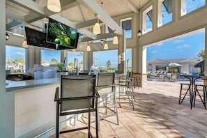 A bar area with a TV, chairs, and a view of the ocean.