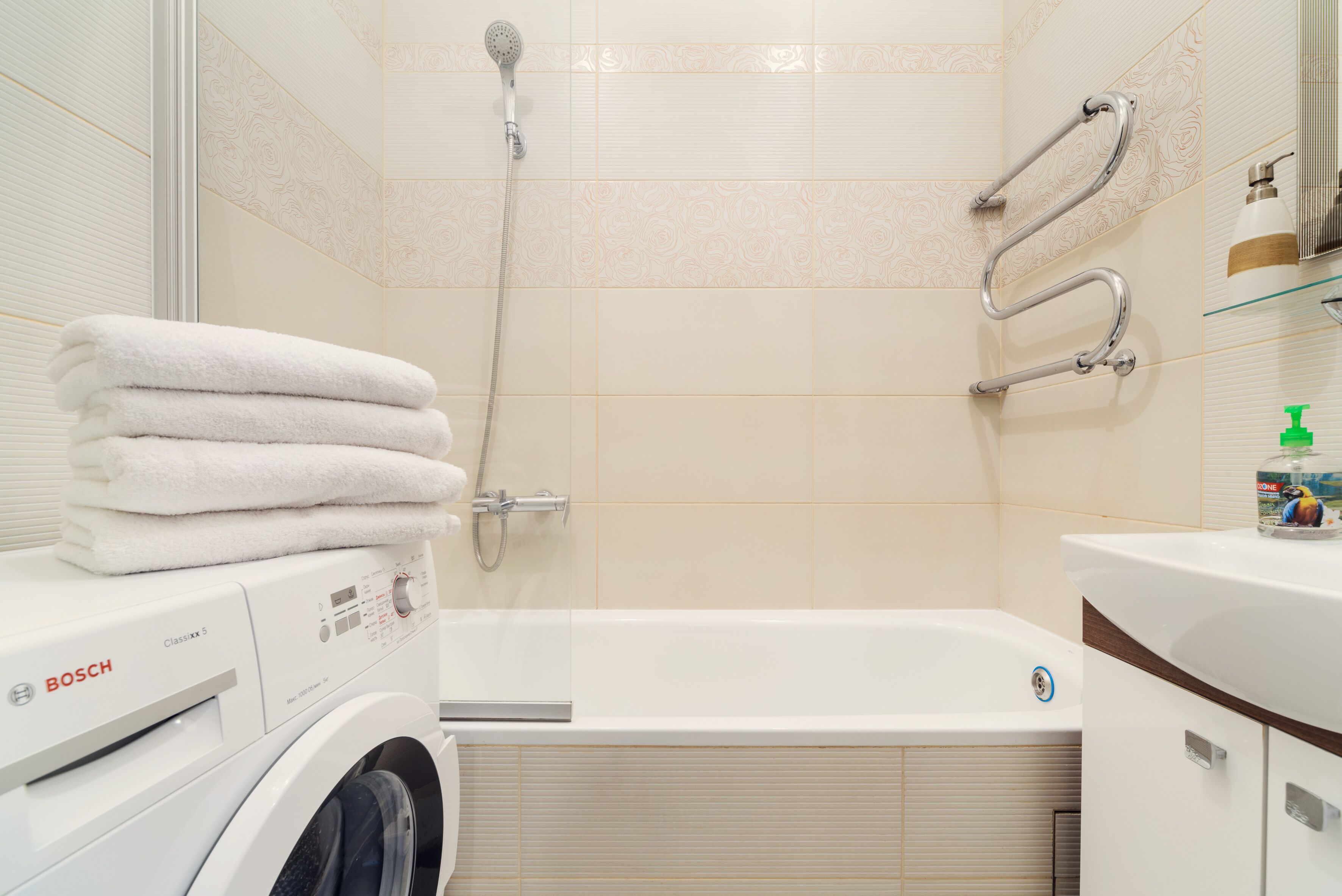 A modern bathroom with a Bosch washing machine, a bathtub, and a shower with grab bars.